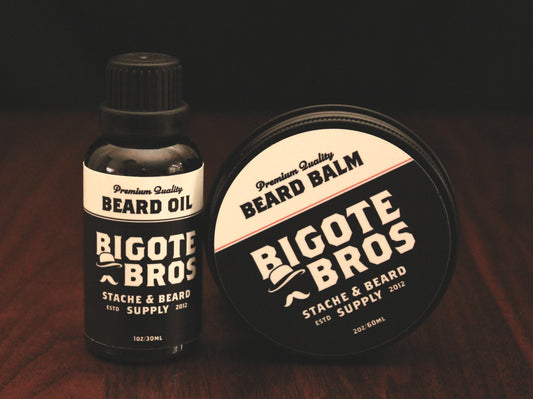 A small bottle of beard oil standing upright right next to a round tin which is also propped upright so that the label can be viewed clearly. Both are standing upright on a wooden surface against a black backdrop.